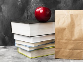 Pile of various books, red apple and package of lunch on dark background