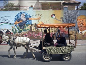 Palestinians ride in a donkey cart past graffiti showing U.S. President Donald Trump with a footprint on his face and Arabic that reads, "For al-Quds (Jerusalem) and the right of return we resist," in Gaza City, Sunday, May 20, 2018.