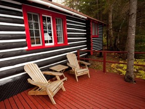 a rustic cabin in the woods with two adirondack chairs on the deck.
