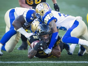 Tiger-Cats running back Sean Thomas Erlington gets to the one-yard line while being tackled by Blue Bombers defensive tackle Cory Johnson (left) and defensive back Marcus Sayles during their game in Hamilton last night. (The Canadian Press)