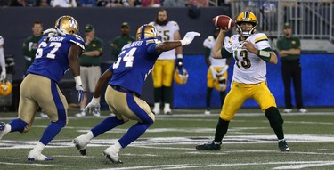 Edmonton Eskimos QB Mike Reilly gets rid of the football under pressure from Winnipeg Blue Bombers DE Tristan Okpalaugo (centre) and DT Cory Johnson during CFL action in Winnipeg on Thurs., June 14, 2018. Kevin King/Winnipeg Sun/Postmedia Network