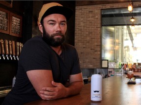 Tyler Birch, owner of Barn Hammer Brewing, sits at his bar in Winnipeg with a can of Barn Hammer brewed beer, a product that has recently become more expensive to produce because of the 10% tariff on aluminum products from the United States.