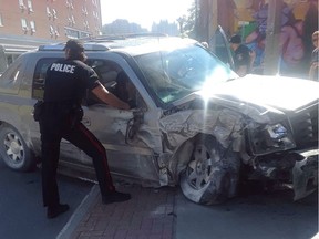 A Winnipeg Police Service officer examines a stolen Cadillac Escalade whose driver led police on a wild chase Friday at around 10:15 a.m., on Furby Street between Sargent Avenue and Ellice Avenue, reaching speeds of over 100 km/h on the sidewalk and damaging several fences and colliding with a business before crashing head-on into an apartment building.