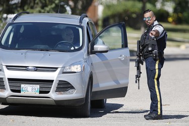 An officer directs traffic in Neepawa, Man., on Thursday, August 30, 2018 as the RCMP emergency response unit moves in on a home as they search for an alleged suspect in the shooting of a RCMP officer in Onanole, Man. THE CANADIAN PRESS/John Woods