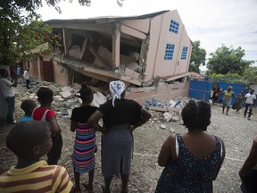 Residents stand looking at a collapsed school damaged by a magnitude 5.9 earthquake the night before, in Gros Morne, Haiti, Sunday, Oct. 7, 2018.
