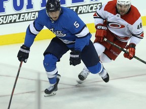 Winnipeg Jets defenceman Dmitry Kulikov (left) skates the puck out of his zone with Carolina Hurricanes forward Jordan Martinook in pursuit in Winnipeg on Sun., Oct. 14, 2018. Kevin King/Winnipeg Sun/Postmedia Network