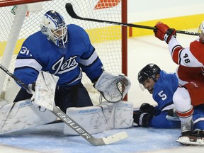 Carolina Hurricanes forward Jordan Martinook (right) falls on Winnipeg Jets defenceman Dmitry Kulikov while swinging at a loose puck in front of goaltender Laurent Brossoit on Sunday night in Winnipeg. Brossoit made 42 saves in his first start of the season. (Kevin King/Winnipeg Sun)