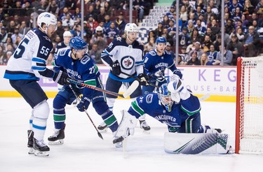 Vancouver Canucks goalie Jacob Markstrom, front right, of Sweden, makes a glove save to stop Winnipeg Jets' Mark Scheifele (55) as Kyle Connor, third left, and Vancouver's Ben Hutton (27) and Troy Stecher (51) watch during the first period of an NHL hockey game in Vancouver, on Monday November 19, 2018. THE CANADIAN PRESS/Darryl Dyck