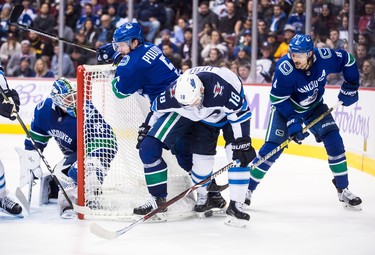 Winnipeg Jets' Bryan Little (18) battles for the puck against Vancouver Canucks' Derrick Pouliot (5) and Chris Tanev (8) behind goalie Jacob Markstrom, of Sweden, during the third period of an NHL hockey game in Vancouver, on Monday November 19, 2018. THE CANADIAN PRESS/Darryl Dyck