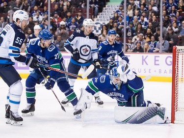 Vancouver Canucks goalie Jacob Markstrom, front right, of Sweden, makes a glove save to stop Winnipeg Jets' Mark Scheifele (55) as Kyle Connor, third left, and Vancouver's Ben Hutton (27) and Troy Stecher (51) watch during the first period of an NHL hockey game in Vancouver, on Monday November 19, 2018. THE CANADIAN PRESS/Darryl Dyck ORG XMIT: VCRD102