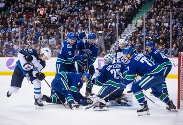 Winnipeg Jets' Kyle Connor (81) digs for the puck under Vancouver Canucks' Chris Tanev (8) in front of goalie Jacob Markstrom (25), of Sweden, as Jake Virtanen (18), Derrick Pouliot (5), Nikolay Goldobin (77), of Russia, Elias Pettersson (40), of Sweden, and Winnipeg's Bryan Little (18) watch during the third period of an NHL hockey game in Vancouver, on Monday November 19, 2018. THE CANADIAN PRESS/Darryl Dyck