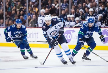 Winnipeg Jets' Blake Wheeler (26) skates with the puck while being watched by Vancouver Canucks' Markus Granlund, back left, of Finland, and Tim Schaller during the third period of an NHL hockey game in Vancouver, on Monday November 19, 2018. THE CANADIAN PRESS/Darryl Dyck