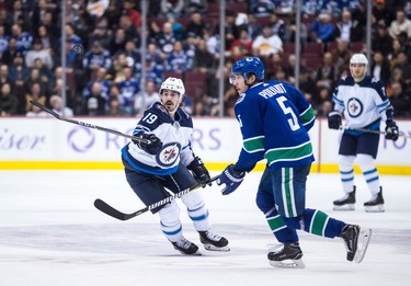 Winnipeg Jets' Nic Petan (19) reaches for the puck in front of Vancouver Canucks' Derrick Pouliot (5) during the first period of an NHL hockey game in Vancouver, on Monday November 19, 2018. THE CANADIAN PRESS/Darryl Dyck