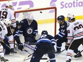 A shot from Chicago Blackhawks forward Alex DeBrincat (left) pops up in the air in front of Winnipeg Jets goaltender Connor Hellebuyck late in the third period last night. (Kevin King/Winnipeg Sun)