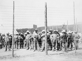 Prisoners stand behind a barbed wire fence at the Castle Mountain internment camp in 1915. Most were Ukrainians.