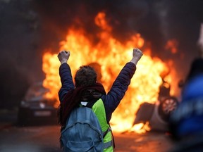 A protester gestures in front of a burning vehicle as "yellow vests" (Gilets jaunes) protesters demonstrate against rising oil prices and living costs in Paris on Saturday, Dec. 1, 2018.
