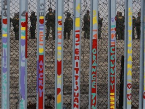 U.S. Border Patrol agents stand guard on the other side of the border in San Diego as they prepare for the arrival of hundreds of pro-migration protestors, seen through the border fence from Tijuana, Mexico, Monday, Dec. 10, 2018.