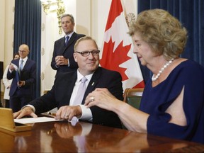 Scott Fielding, MLA for Kirkfield Park, centre signs documents with Lieutenant Governor Janice Filmon after he is sworn into cabinet as the new minister of Finance and minister responsible for the civil service during Premier Brian Pallister's cabinet shuffle announced at the Manitoba Legislature in Winnipeg on August 1, 2018. The Manitoba government is making its tax credit for film and video productions permanent. Sport, Culture and Heritage Minister Cathy Cox says the credit, which was set to expire at the end of this year, has attracted projects and boosted the economy. Finance Minister Scott Fielding says the province will offer more to the film and video industry in the spring budget, which is expected in March, but he would not reveal details. THE CANADIAN PRESS/John Woods