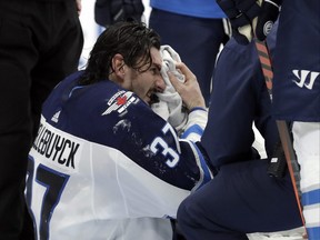 Jets goaltender Connor Hellebuyck wipes his face after getting cut after a shot by the Lightning hit him on the mask during the second period on Tuesday night in Tampa. (AP PHOTO)
