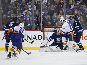 New York Islanders’ Anders Lee (27) tips a shot by Ryan Pulock’s (6) shot past Jets goaltender Connor Hellebuyck during the second period of Thursday’s game in Winnipeg. The hosts allowed two goals in the final two minutes en route to the crushing defeat. (THE CANADIAN PRESS)