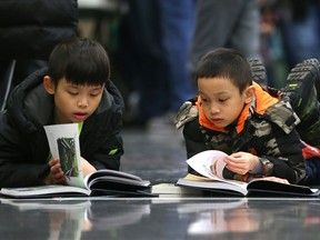 Jensen Wu (right), 6, peeks at the book his brother Jeremy, 7, is reading during a Family Literacy Fun Day event at Lord Roberts Community Centre in Winnipeg on Sunday.