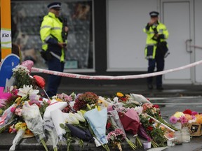 Flower rest at a road block while two police officers stand guard next to the makeshift memorial near the Linwood mosque in Christchurch, New Zealand, on March 16, 2019. (AP Photo/Vincent Thian)