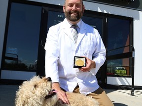Dr. Jonas Watson and his dog Carlin, a Labradoodle he rescued from a Manitoba puppy mill, pose with the medal he was awarded by the World Veterinary Association, at Tuxedo Animal Hospital on Corydon Avenue in Winnipeg, on Monday.