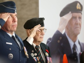 Attendees salute in front of a poster depicting a veteran saluting at an event Tuesday at the Manitoba Legislature to commemorate D-Day.