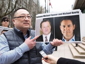 In this file photo taken on March 6, 2019, Louis Huang of Vancouver Freedom and Democracy for China holds photos of Canadians Michael Spavor and Michael Kovrig, who are being detained by China, in Vancouver, Canada.