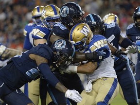 Toronto Argonauts defenders Jonathan Dowling (left) and Freddie Bishop III stop Winnipeg Blue Bombers running back Andrew Harris during Thursday's game. (THE CANADIAN PRESS)