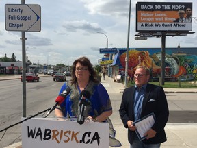 PC candidates Colleen Mayer (St. Vital) and Scott Fielding (Kirkfield Park) address media at a press conference on Portage Avenue in Winnipeg on Friday, in front of a billboard talking about the NDP and former Premier Greg Selinger and current leader Wab Kinew.
