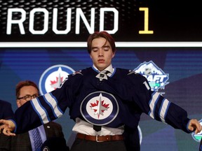 Ville Heinola pulls on his Jets jersey after being selected 20th overall by Winnipeg at the NHL draft this summer. GETTY IMAGES