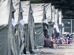 Asylum seekers sit in front of their tent in a temporary camp, Tuesday, August 15, 2017 near Saint-Bernard-de-Lacolle, Que. Winterized trailers will soon be replacing the tents providing temporary shelter to asylum-seekers who have crossed the Quebec-U.S. border, even as the number of irregular border crossings continues to drop. THE CANADIAN PRESS/Paul Chiasson ORG XMIT: cpt106