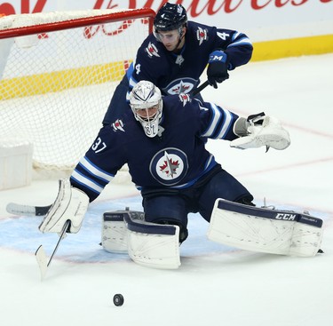 Winnipeg Jets goaltender Connor Hellebuyck eyes a loose puck with defenceman Neal Pionk in his crease during NHL action against the Minnesota Wild in Winnipeg on Thurs., Oct. 10, 2019. Kevin King/Winnipeg Sun/Postmedia Network