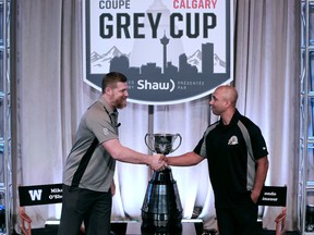 Blue Bombers head coach Mike O’Shea (left) and Tiger-Cats head coach Orlondo Steinauer shake hands before a news conference in Calgary yesterday.  Gavin Young/Postmedia network