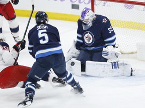 Jets goaltender Laurent Brossoit stops a shot by Columbus Blue Jackets’ Eric Robinson as Jets’ Luca Sbisa defends during the first period last night in Winnipeg. Brossoit left the game with cramps. (John Woods/ The Canadian Press)