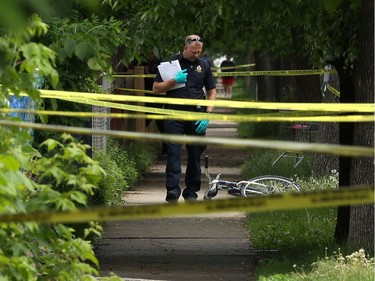 An investigator examines a bicycle found across the street from the main entrance to John M. King School, an elementary school on Agnes Street in Winnipeg, on Mon., June 17, 2019. Police are investigating a homicide after an adult male was shot early Monday morning. Kevin King/Winnipeg Sun/Postmedia Network ORG XMIT: POS1906171335064148