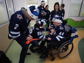 Nathan Beaulieu (centre) signs the jersey of Zack Kuffel (right) and Anthony Bitetto signs his stick as mother Janique watches during the Winnipeg Jets annual holiday hospital visit, at the Rehabilitation Centre for Children on Notre Dame Avenue in Winnipeg, on Monday.