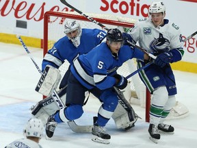 Winnipeg Jets defenceman Luca Sbisa (centre) ties up Vancouver Canucks forward Jake Virtanen in front of goaltender Connor Hellebuyck in Winnipeg on Tues., Jan. 14, 2020. Kevin King/Winnipeg Sun/Postmedia Network