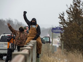 A demonstrator raises his fist as he sits on a bridge overlooking an encampment of the Tyendinaga Mohawk Territory, set up in support of the Wet'suwet'en Nation who are trying to stop construction of B.C.'s Coastal GasLink pipeline, in Tyendinaga, Ont., Feb. 26, 2020. (REUTERS/Alex Filipe)