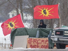 A protester stands between Mohawk Warrior Society flags at a rail blockade on the 10th day of demonstration in Tyendinaga, near Belleville, Ont., Sunday, Feb. 16, 2020.