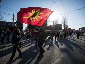 A man carries a Mohawk Warrior Society flag as protesters march on East Hastings St. in support of Wet'suwet'en Nation hereditary chiefs attempting to halt construction of a natural gas pipeline on their traditional territories, in Vancouver, B.C., Tuesday, Feb. 18, 2020.