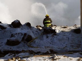 A firefighter sits on a mudhill to spray hotspots at the scene of an early-morning fire at a condominium complex on Philip Lee Drive in the West Transcona area of Winnipeg on Sunday.