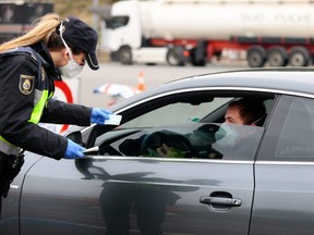 A Spanish police officer checks the identity papers of a driver at a checkpoint near tolls at the La Jonquera crossing between France and Spain on Tuesday, March 17, 2020.