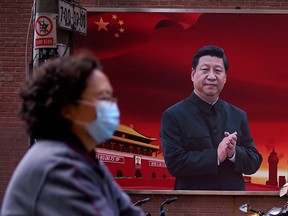 A woman wearing a protective mask is seen past a portrait of Chinese President Xi Jinping on a street as the country is hit by an outbreak of the coronavirus, in Shanghai, March 12, 2020. (REUTERS/Aly Song/File Photo)