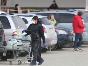 Shoppers wearing gloves and masks with groceries at  a grocery shop on St.James Street. Social distancing is being practised in the line up in the background on Wednesday, April 8, 2020.