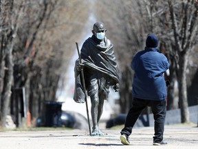 A man takes a picture of the Mahatma Gandhi statue, wearing a surgical mask, at The Forks in Winnipeg on Sunday.