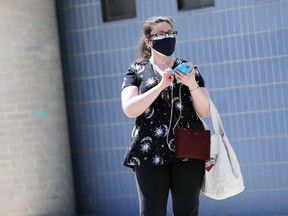 A woman wearing scrubs and a protective mask waits for a bus outside Health Sciences Centre in Winnipeg on Monday.