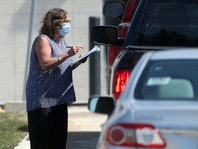 A woman wears a mask and eye protection while approaching vehicles at a COVID-19 testing location on Main Street, in Winnipeg. Friday.