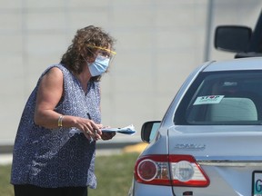 A woman wears a mask and eye protection while approaching vehicles at a Covid-19 testing location on Main Street, in Winnipeg on Friday. For Victoria Day, the Sergeant Tommy Prince Place testing site and assessment clinic in Winnipeg will be open, as will the Bison Drive drive-thru site. Testing locations in Winkler and Selkirk will also be open. All other locations throughout the province will be closed on Monday and reopen on Tuesday.